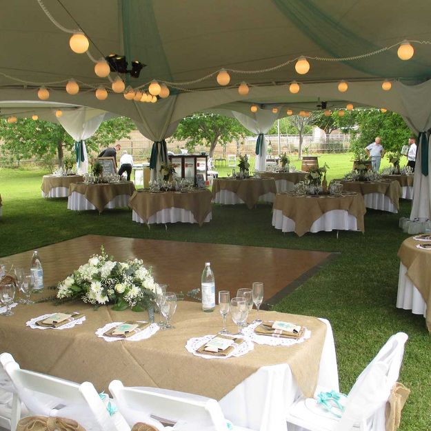 Dance floor centrally located between round guest tables and a rectangular wedding party table under a rental tent.